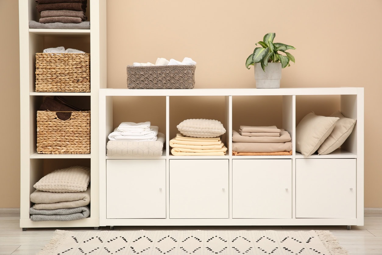 Folded linens and pillows on shelving unit indoors. Home textile storage